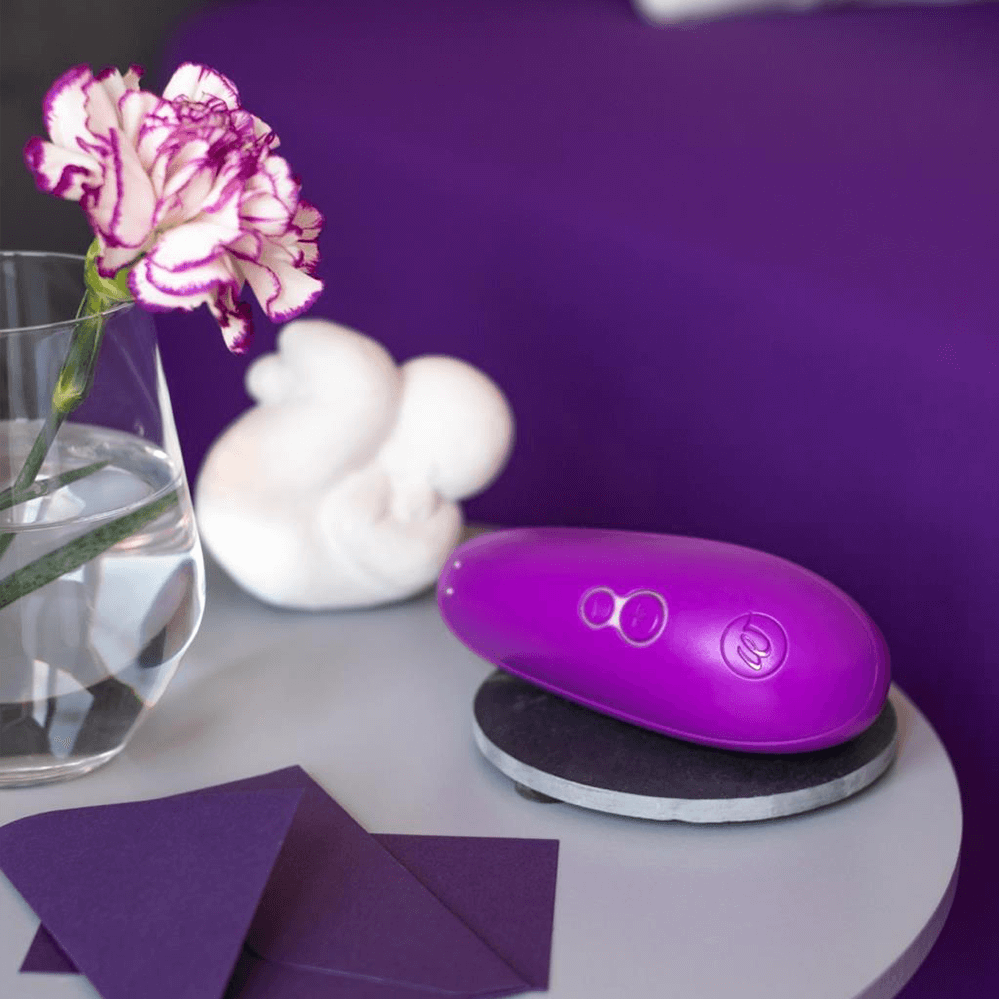 Purple womanizer starlet 3 clitoral vibrator on a table with a flower and decorative items