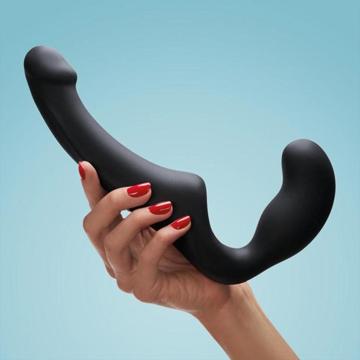 Hand holding a black strp-on sex toy against a light blue background